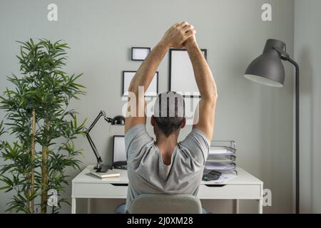 Rückansicht Mann Schreibtisch Stretching während der Arbeit von zu Hause aus. Hochwertiges, schönes Fotokonzept Stockfoto