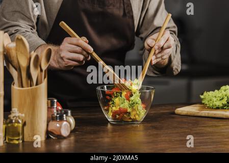 Mid-Shot-Koch, der Salatzutaten mischt. Hochwertige Fotos Stockfoto