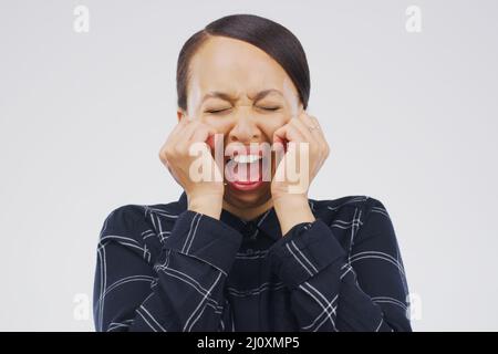 Kannst du mich hören? Studioaufnahme einer jungen Frau, die weint, während sie vor einem grauen Hintergrund steht. Stockfoto