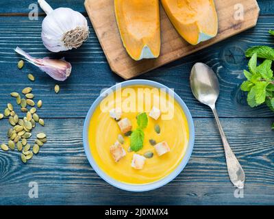 Von Kürbis cremige Suppe mit Croutons und Samen auf dunkelblauem Hintergrund Holz, Knoblauch, Minze, kürbisscheiben. Ansicht von oben. Stockfoto