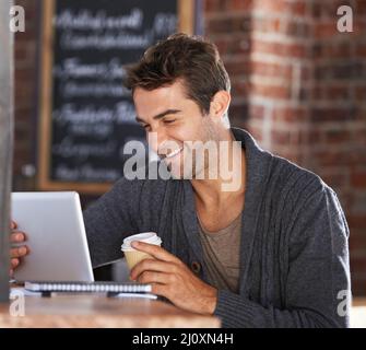 Tolles WiFi und guten Kaffee. Ein junger Mann, der an einem digitalen Tablet arbeitet und einen Kaffee in einem Restaurant hält. Stockfoto