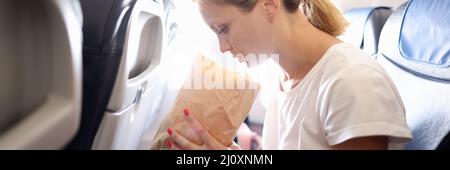 Junge Frau, die im Flugzeug fliegt und in einen Papiersack atmet Stockfoto