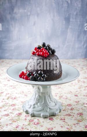 Traditioneller australisches Pflaumenpudding mit frischen Waldbeeren, der als Nahaufnahme auf einem Dessertteller mit Design auf einem Tisch mit Kopie angeboten wird Stockfoto