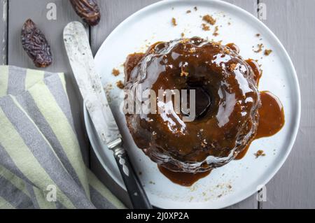 Traditioneller englischer klebriger Toffee-Pudding mit Karamell-Glasur diente als Draufsicht auf einem Design-Teller Stockfoto