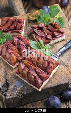 Der traditionelle deutsche Zwetschgenkuchen mit geschnittenen Pflaumen diente als Nahaufnahme auf einem rustikalen Holzbrett Stockfoto