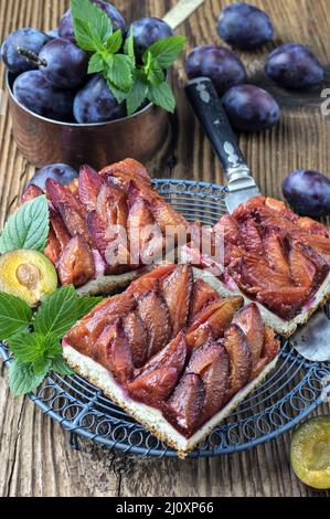 Der traditionelle deutsche Zwetschgenkuchen mit geschnittenen Pflaumen diente als Nahaufnahme auf einem rustikalen Holzbrett Stockfoto