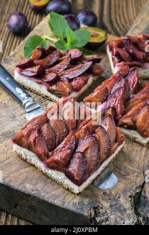 Der traditionelle deutsche Zwetschgenkuchen mit geschnittenen Pflaumen diente als Nahaufnahme auf einem rustikalen Holzbrett Stockfoto