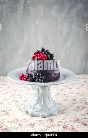 Traditioneller australisches Pflaumenpudding mit frischen Waldbeeren, der als Nahaufnahme auf einem Dessertteller mit Design auf einem Tisch mit Kopie angeboten wird Stockfoto