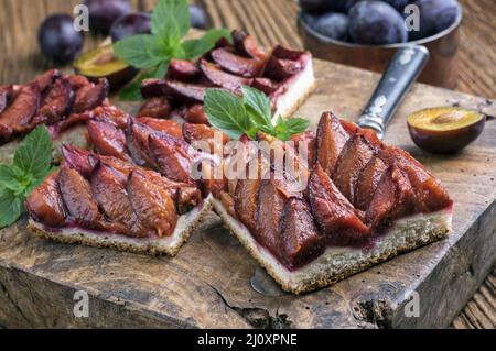 Der traditionelle deutsche Zwetschgenkuchen mit geschnittenen Pflaumen diente als Nahaufnahme auf einem rustikalen Holzbrett Stockfoto