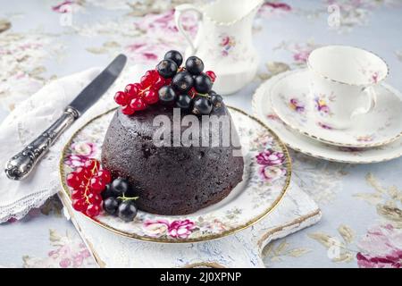 Traditioneller australischer Pflaumenpudding mit frischen Waldbeeren, der als Nahaufnahme auf einem Dessertteller angeboten wird Stockfoto