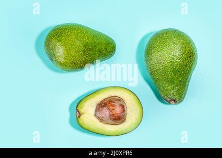 Ganze und aufgeschnittene Avocado auf blauem flachem Hintergrund. Einfaches Avocado-Muster, Draufsicht. Pop-Art-Design, kreatives sommerliches Food-Konzept. Frisches grünes avo Stockfoto