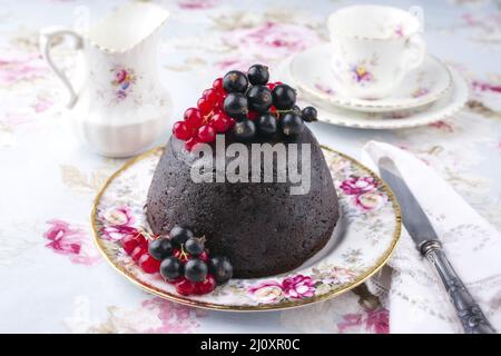 Traditioneller australischer Pflaumenpudding mit frischen Waldbeeren, der als Nahaufnahme auf einem Dessertteller angeboten wird Stockfoto