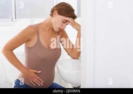 Die Schmerzen und Schmerzen der Schwangerschaft. Eine Schwangerin, die im Badezimmer mit Morgenkrankheit zu kämpfen hat. Stockfoto