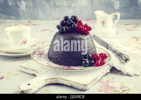 Traditioneller australischer Pflaumenpudding mit frischen Waldbeeren, der als Nahaufnahme auf einem Dessertteller angeboten wird - Jahrgang Stockfoto