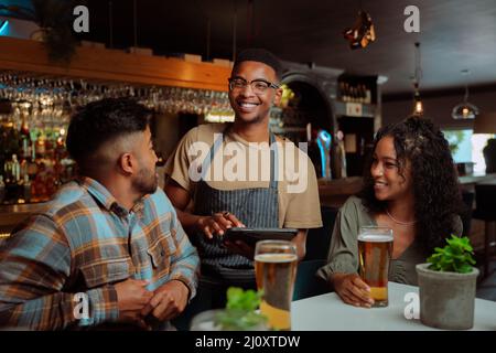 Afroamerikanischer Kellner, der Paare und Freunde im Restaurant bedient Stockfoto