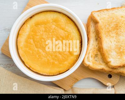 Weißes rundes Ramekin mit Omelett aus Eiern und Milch im Ofen, mit Kruste, auf weißem Holztisch, Draufsicht. Stockfoto