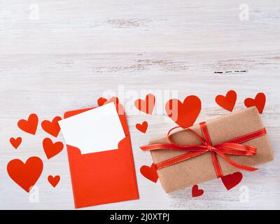 Symbol des Valentinstag - Geschenkbox aus kraftbraunem Papier mit rotem Band, Umschlag mit einem sauberen leeren Blatt Papier auf weißem b Stockfoto