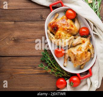 Zwei Kadaver gebratenes Huhn in einer Schüssel, gebackene Chucks im Ofen mit Tomaten, mit knuspriger Kruste, auf dunkelbraunem rustikalem Holztab Stockfoto