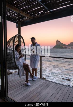 Ein Paar, ein Mann und eine Frau, die während des Sonnenaufgangs auf dem Balkon Kaffee trinken, während eines Urlaubs in Kapstadt, Südafrika Stockfoto