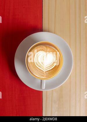 Kaffeebecher auf Holztisch. Von oben gesehen Tasse Kaffee auf Holztisch. Heißer Kaffee in weißer Tasse auf Holztisch aus nächster Nähe. Coffee Latte Art Herz formt sich in wh Stockfoto