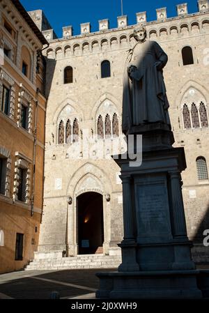 Siena, Italien - 2022. Februar 10: Sallustio Bandini Statue, modelliert von Tito Sarrocchi (1882). Im Hintergrund das Bankgebäude des Monte dei Paschi. Stockfoto