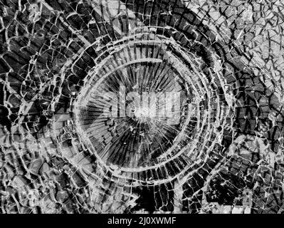 Zerbrochenes Glas. Rundes Loch mit radialen Rissen im Glas. Runde weiße Risse in Glas auf schwarzem Hintergrund Stockfoto
