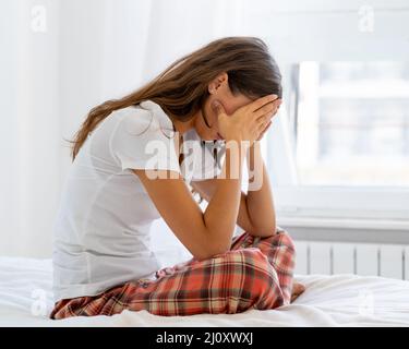 Frau schaut ängstlich weg, berührt Stirn und Haar mit der Hand. Stockfoto