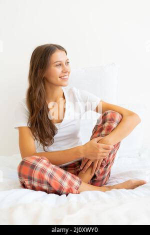 Schöne junge Frau ohne Make-up auf dem Bett sitzen und wegschauen nach dem Aufwachen. Stockfoto