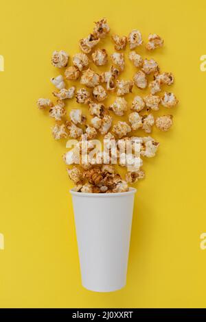 Karamell-Popcorn aus dem Papierbecher auf gelbem Hintergrund, Draufsicht Nahaufnahme, süße Snacks Stockfoto