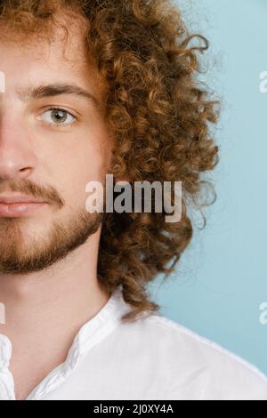 Junger lockiger Mann mit Ingwerhaar, der posiert und isoliert auf blauem Hintergrund auf die Kamera schaut Stockfoto