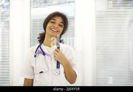 Glückliche afroamerikanische Ärztin in medizinischer Uniform mit Stethoskop um den Hals lächelnd vor der Kamera Stockfoto