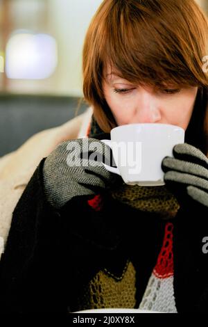 Gefrorenes Mädchen wärmt sich mit heißem Getränk. Hände in Handschuhen halten Tasse Kaffee oder Tee Stockfoto