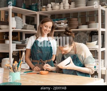 Frau, die Keramik macht. Attraktive, qualifizierte junge Dame im Schürze, die am Tisch steht und lehrt Stockfoto