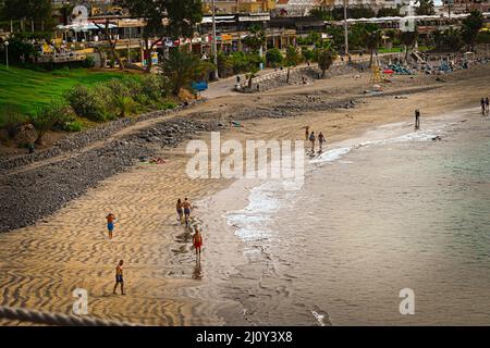 Ein Blick auf einen Strand mit importiertem Sand, der mit dem natürlichen Vulkansand in Costa Adeje, Teneriffa, vermischt ist und Urlauber die Sonne genießen Stockfoto