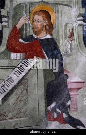 Der rothaarige Heilige Matthew, der Evangelist, sitzt an einem Schreibtisch und schreibt sein Evangelium im spätgotischen Piemont-Fresko-Zyklus von 1400s. An der Decke in der Kirche des ehemaligen Franziskanerklosters in Susa, Piemont, Italien. Stockfoto