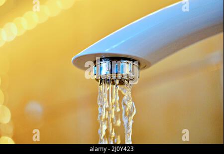 Das Wasser läuft aus einem weißen Plastikwasserhahn. Nahaufnahme Stockfoto