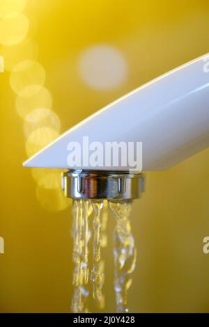 Das Wasser läuft aus einem weißen Plastikwasserhahn. Nahaufnahme Stockfoto