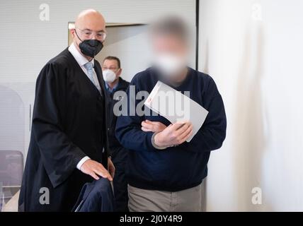 Bad Kreuznach, Deutschland. 21. März 2022. Der Angeklagte wird in Handschellen in den Gerichtssaal gebracht. Auf der linken Seite ist sein Anwalt Alexander Klein. Der Mann soll im vergangenen Jahr auf den Mitarbeiter einer Tankstelle in Bad Kreuznach geschossen haben, nachdem er ihm darauf hingewiesen hatte, dass er eine Coronamaske tragen müsse. Kredit: Boris Roessler/dpa - ACHTUNG: Der Angeklagte wurde durch Befehl des Gerichts/dpa/Alamy Live News pixeliert Stockfoto