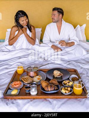 Mann und Frau frühstückten im Bett, Paar frühstückten mit Kaffeebrot und Obst im Schlafzimmer Stockfoto