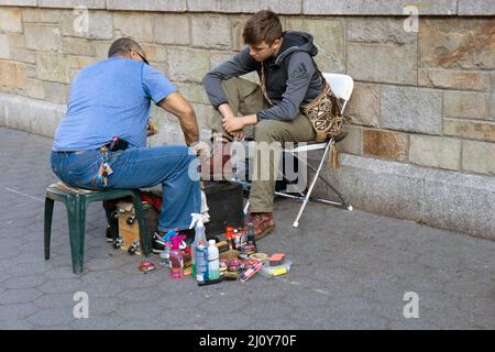 Ein Mann mittleren Alters, der glänzte, polierte im Union Square Park in Manhattan, New York City, die Doc Marten-Stiefel eines jungen Mannes. Stockfoto