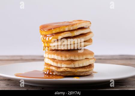 Stapel von acht Pfannkuchen mit Sirup serviert in Teller auf dem Tisch vor grauem Hintergrund Stockfoto