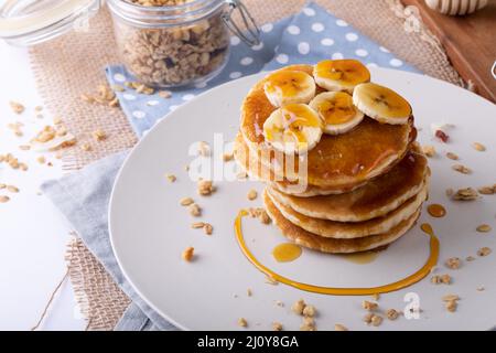 Blick aus der Perspektive auf Pfannkuchen, serviert mit Bananenscheiben, Hafer und Honig auf dem Teller auf Serviette Stockfoto