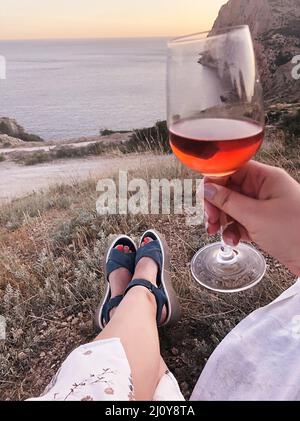 Eine kurze Aufnahme einer Frau mit einem Glas Rotwein und herrlichem Meerblick und Sonnenuntergang Stockfoto