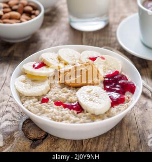 Gesundes Frühstück am Morgen - Haferflocken mit Scheiben von Bananen, himbeermarmelade und Erdnussbutter. Von der Seite. Stockfoto