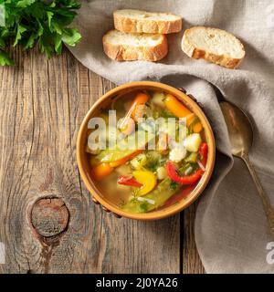 Helle vegetarische Suppe mit Frühlingsgemüse. Draufsicht, brauner rustikaler Holzhintergrund, Leinenserviette. Stockfoto