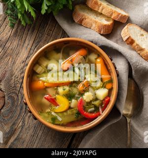 Helle vegetarische Suppe mit Frühlingsgemüse. Draufsicht, brauner rustikaler Holzhintergrund, Leinenserviette. Stockfoto