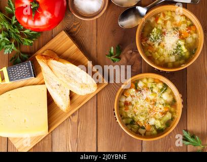 Zwei Schüsseln Minestrone mit Käse auf Schneidebrett und Gemüse Stockfoto