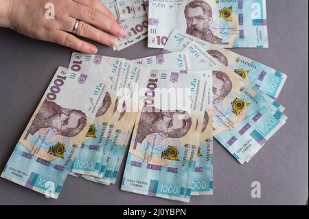 Nahaufnahme einer weiblichen Hand, die Geld vor grauem Hintergrund zählt. Erwachsene weibliche Inhaber ukrainischer Banknoten. Bargeld im Wert von 1.000 Griwna. Stockfoto