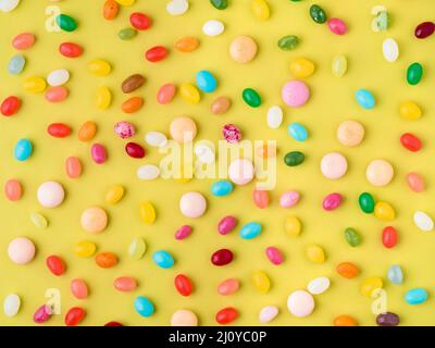 Viele verstreute bunte Süßigkeiten, Bonbons, Lutscher auf gelben Hintergrund, Ansicht von oben Stockfoto