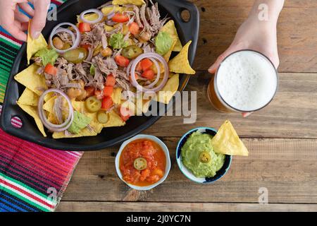 Tablett mit Nachos mit Fleisch und Hand ein Glas Bier zu halten. Schüsseln mit Salsa. Draufsicht. Speicherplatz kopieren. Stockfoto